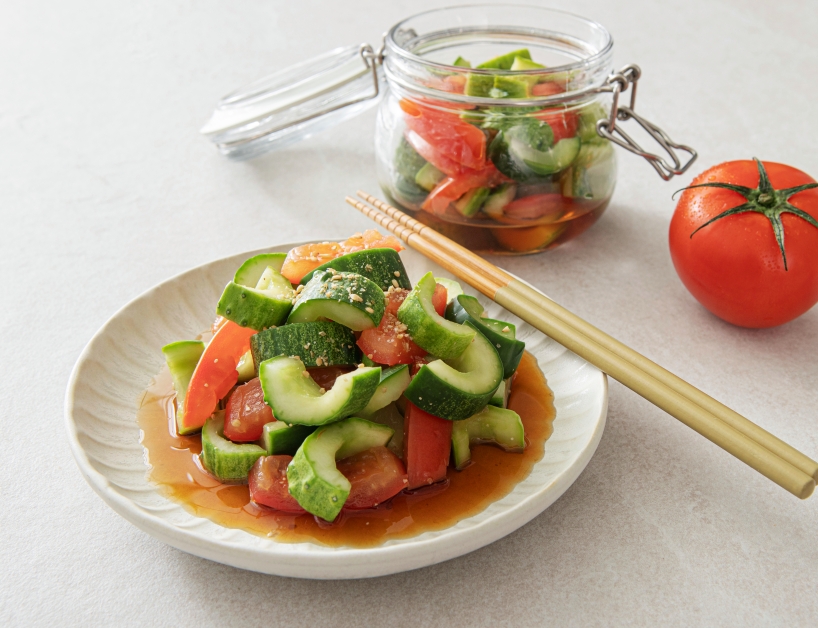 사진에는 오이와 토마토로 만든 상큼한 무침이 담겨 있습니다.
앞쪽 접시에는 큼직하게 썬 오이와 토마토가 간장 소스와 함께 담겨 있고, 위에는 참깨가 뿌려져 있습니다.
옆에는 황금빛 젓가락이 놓여 있어 깔끔한 식탁 분위기를 줍니다.
뒷편에는 같은 무침이 담긴 유리병과 신선한 통토마토가 보입니다.
전체적으로 신선하고 가벼운 여름 반찬의 느낌이 강조됩니다.